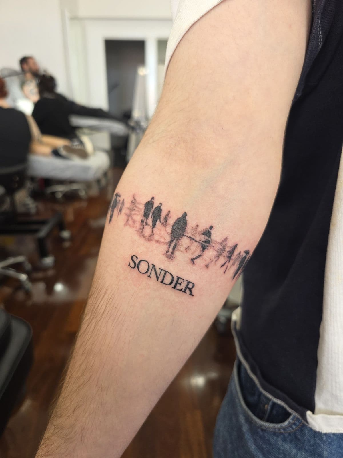 Silhouette band of figures with SONDER lettering, forearm
